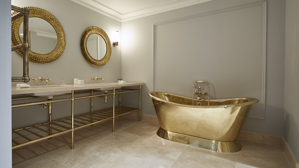 Ein Badezimmer mit goldener Badewanne auf hellbeigen Fliesen